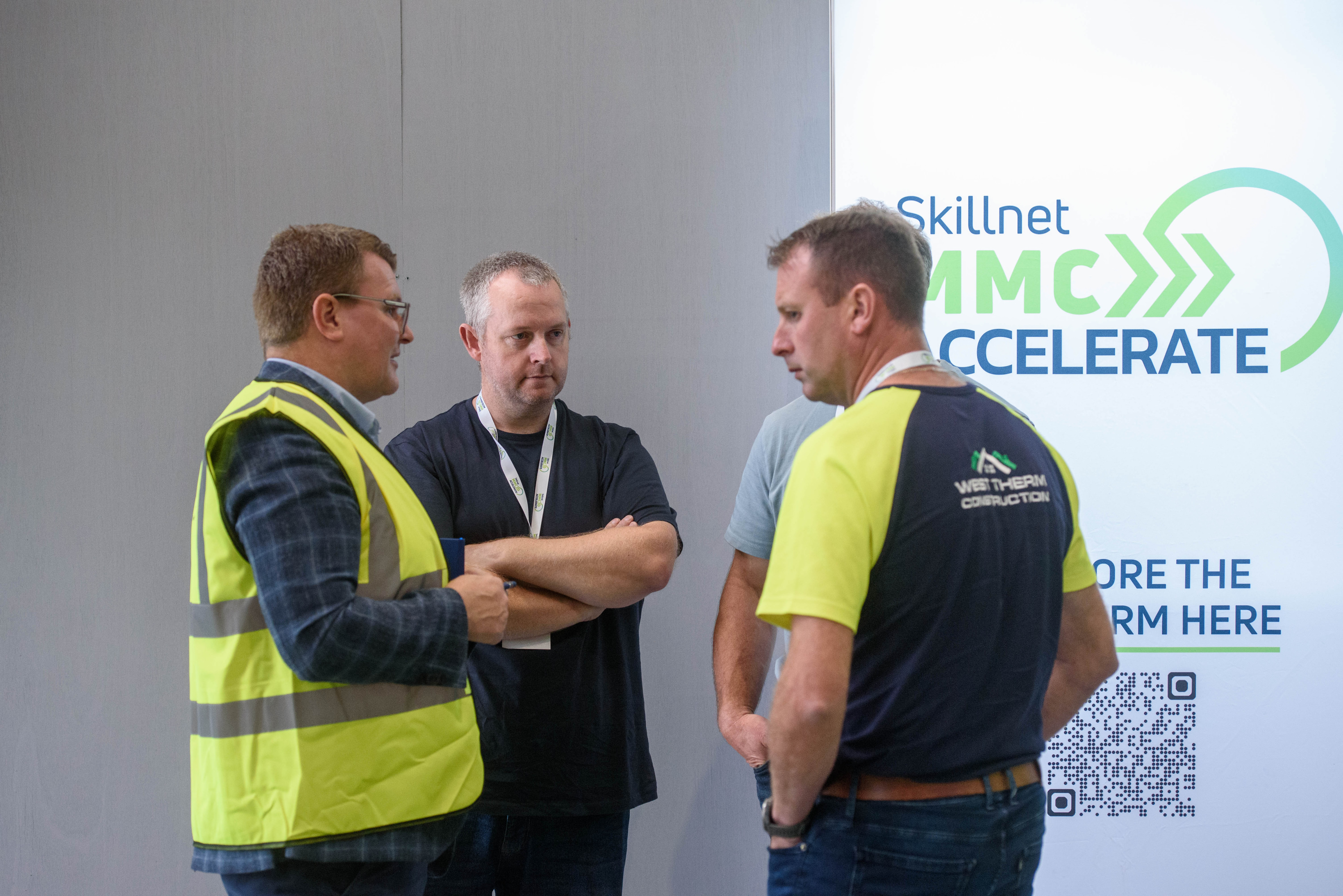 Three people in safety vests having a conversation in front of an "Accelerate" event sign.