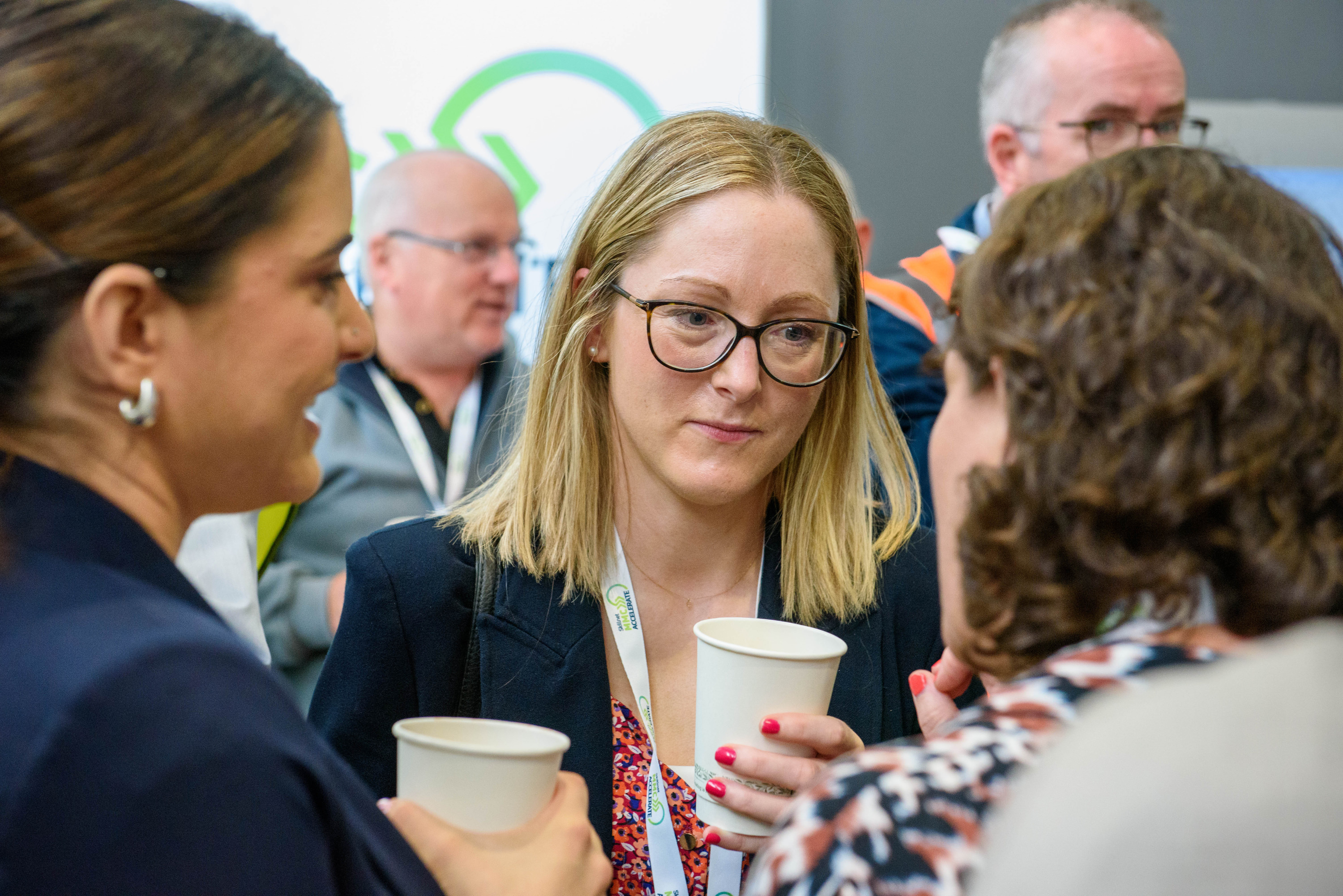 A person with glasses in focus during a professional conference or networking event.