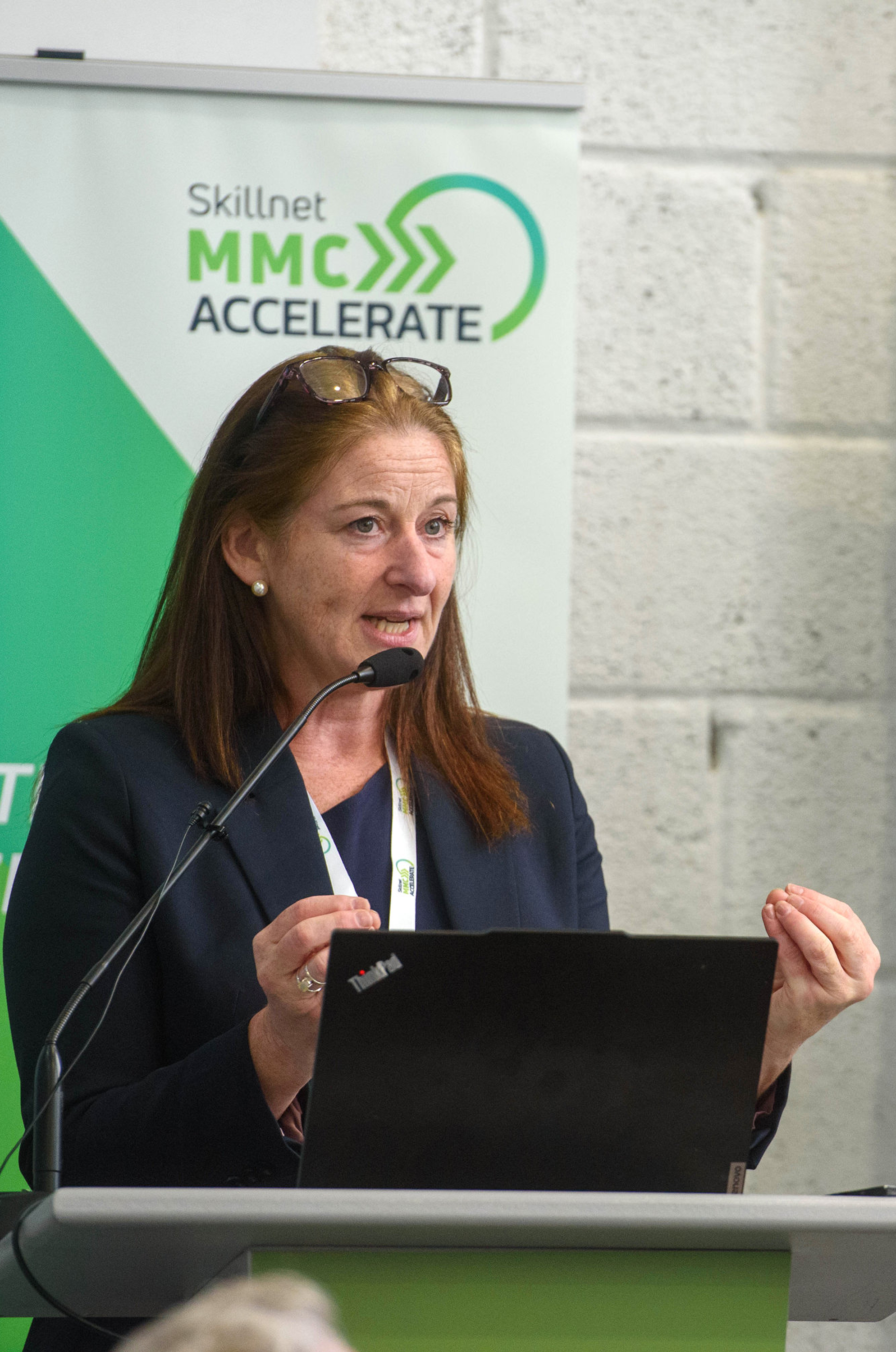 A woman in a suit speaking at a podium with a green MimOSA logo banner in the background.