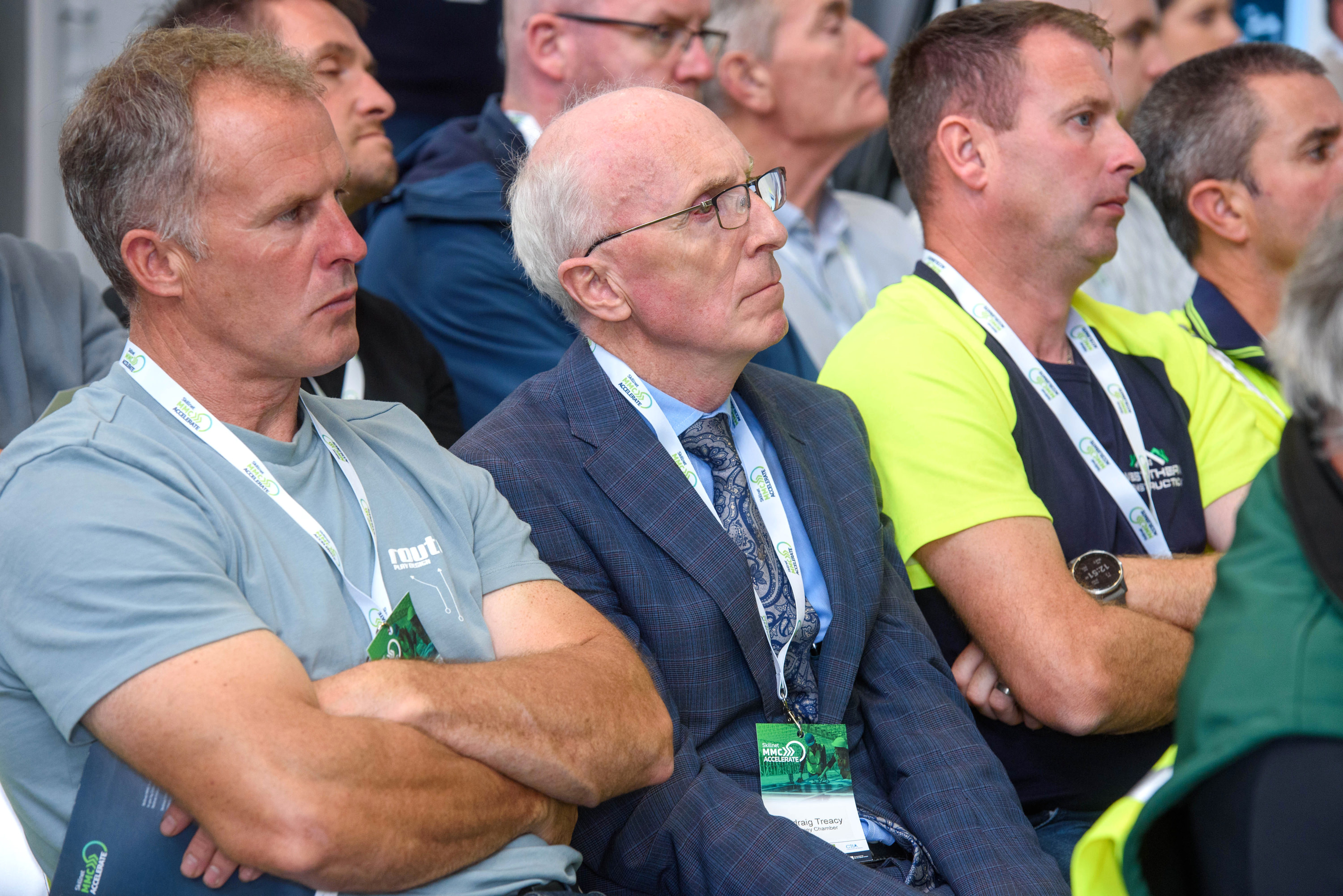 Group of spectators watching an event, with one person wearing a yellow safety vest.