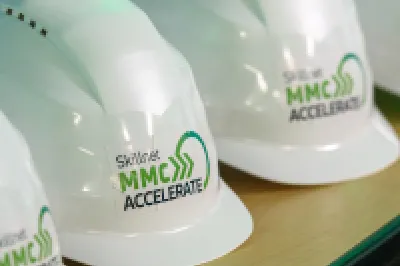 White hard hats are placed on the table, featuring the Skillnet MMC Accelerate logo.
