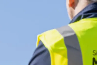 Person wearing a hard hat and high-vis vest looking at a construction site.