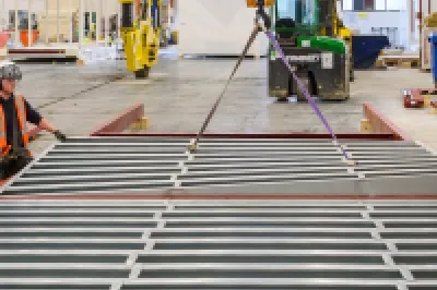 Three people in high vis vests inspect metal frames lying on the ground.