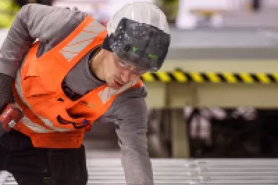 A male in a high vis jacket and hard hat holding a power tool crouches over a pallet.
