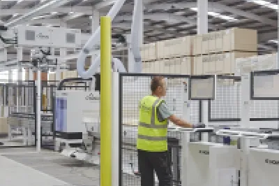 Person in high-vis vest operating a robotic system inside a construction manufacturing facility.