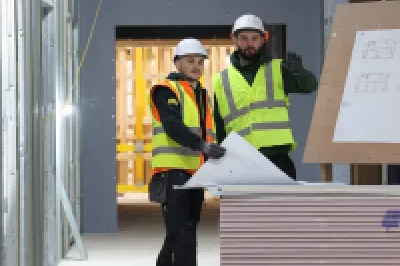 Two people in high-vis vests and hard hats reviewing plans inside a construction unit.