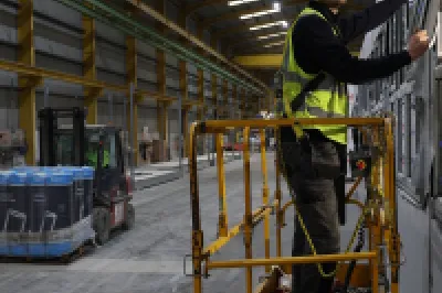 A male in a hard hat and high vis vest stands on a yellow scissor lift to test a window.