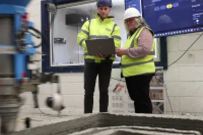 Two people operating a 3D concrete printing machine.