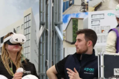 Two people sitting at a table, with the male watching as the female uses a VR headset.