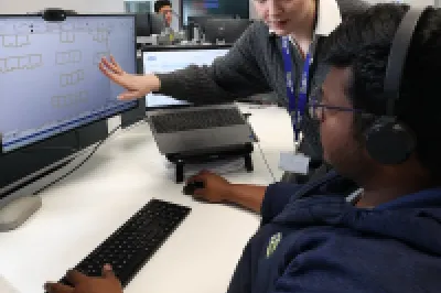 Two people are at a workstation, one is showing construction drawings on the screen to the other.