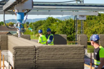 Workers operating a 3D concrete printing machine on a сonstruction site.