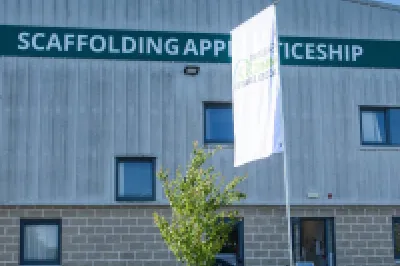 Grey building with the sign 'Scaffolding Apprenticeship' and two white flags showing the Skillnet MMС Accelerate logo.