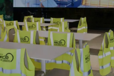 High vis vests with the Skillnet MMC Accelerate logo hang off the back of white chairs around white tables in an event space with a screen in the background.