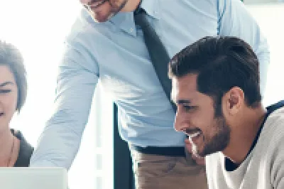 Three colleagues working together in a bright modern office, gathered around a laptop and discussing something on the screen.
