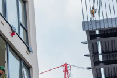 Prefabricated balcony being lifted by crane next to a multi-storey building under construction.