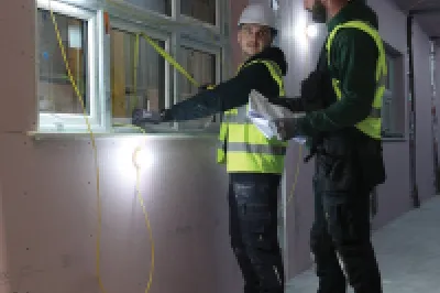 Two people in high-vis vests inspecting a window inside a construction unit