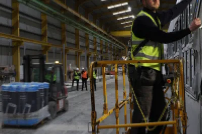 A male with a high vis vest and hard hat stands on a scissor lift to fit a window.