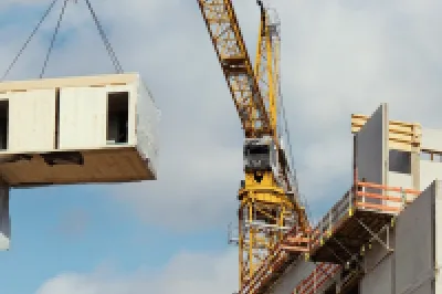 A crane lifts a modular building unit across a construction site.