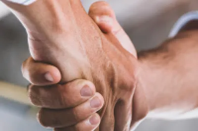 A person in a business shirt shakes hands with a person in a business shirt and high vis vest.