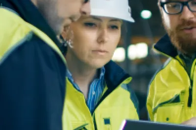 A group of people in hard hats and high vis vests read from a tablet screen.