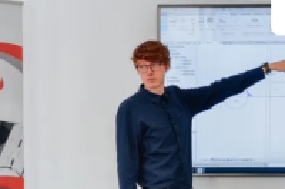 A person is standing next to a screen, pointing at a slide during a training session in a classroom.