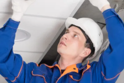 Worker in hard hat installing or inspecting a ceiling smoke detector.