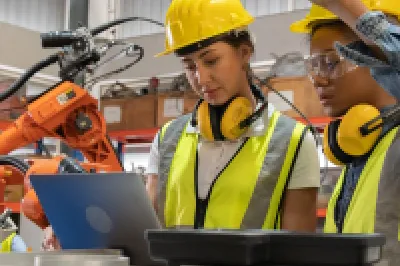 Two workers wearing high-visibility vests and hard hats are working with robotics.