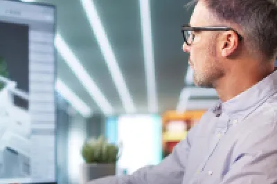 Architect working on 3D building model using multiple computer monitors.