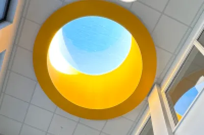 A bright, modern school interior with large windows, a central skylight featuring a yellow circular frame