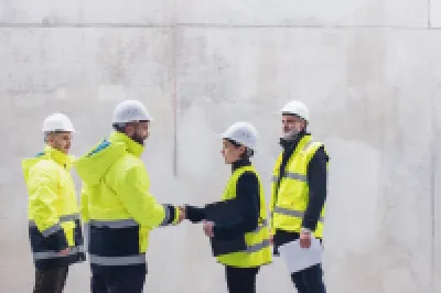 Four construction workers wearing high-visibility jackets and helmets standing and talking near a large concrete wall.
