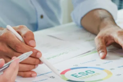Close-up of hands reviewing architectural or technical documents with charts and drawings on a desk, suggesting a collaborative planning or design meeting.