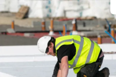 Construction worker in a high-visibility vest and hard hat installing insulation panels on a building site.