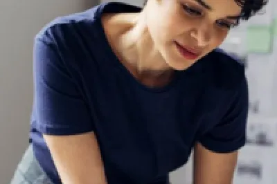 Person reviewing documents at a desk with design plans on the wall in the background.