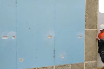 Workers in safety gear installing a large prefabricated wall panel on a construction site, with MMC Eco Homes logo in the corner.