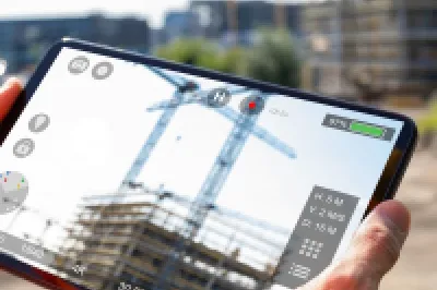 Worker using a tablet to pilot a drone over a construction site, with cranes and a multi-storey building in the background.