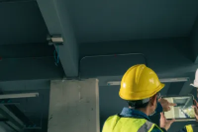 Two construction workers in safety vests and helmets inspecting ceiling installations