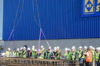 A group of workers in safety vests gathered outside a large blue Midland Steel facility building.