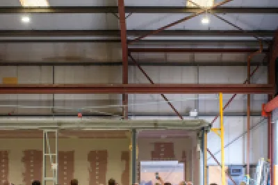 Group of workers in high-visibility vests gathered inside a large industrial warehouse with stacked containers.