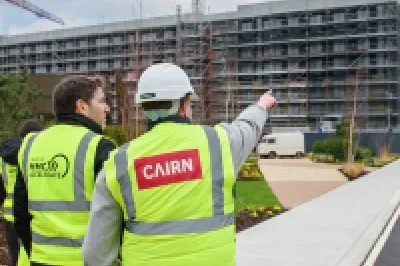 Construction workers in high-visibility vests overlooking a building site with cranes and scaffolding.