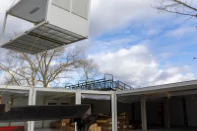 A modular building unit being lifted by a crane at a construction site.