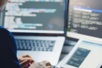 Person working at a desk with multiple screens showing code and data.