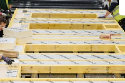 Workers in high-visibility vests assembling insulated timber wall panels inside a modern offsite construction factory.