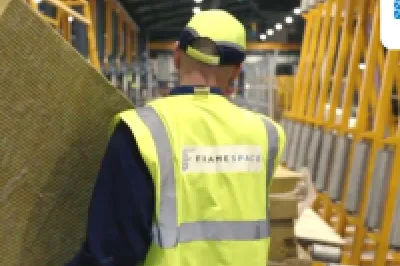 Construction worker in a yellow safety vest handling insulation material inside a building frame.