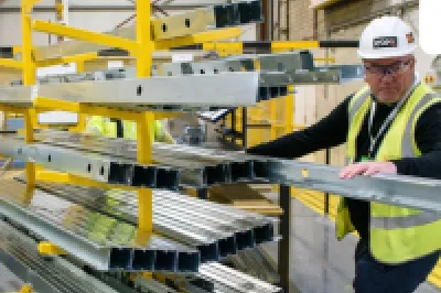 Workers in safety vests inspecting materials on yellow shelving in an industrial warehouse with Remainly logo.