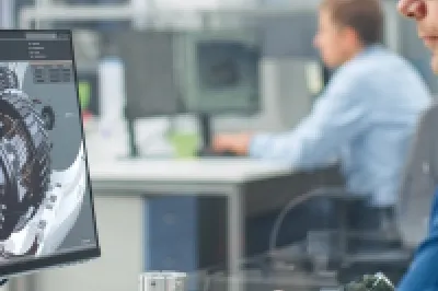 Person working on a computer with engine design or mechanical diagram on screen in an industrial setting.