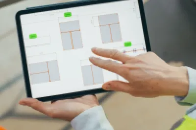 Two construction workers in safety helmets reviewing plans on a tablet at a worksite.