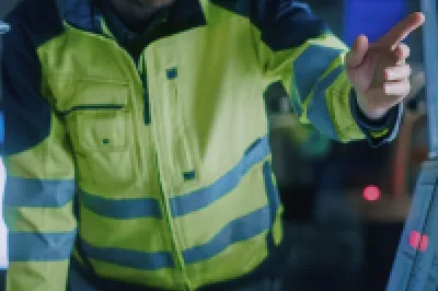 Two workers in hard hats and safety vests examining a digital screen in an industrial setting.