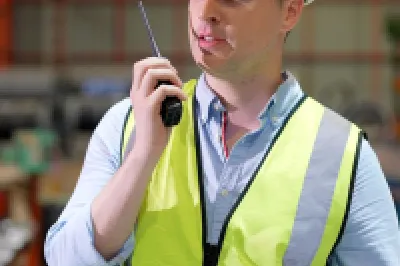 Worker in hard hat and safety vest standing in an industrial warehouse environment.