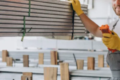 Construction worker in orange helmet reviewing documents in warehouse with stacked building materials.