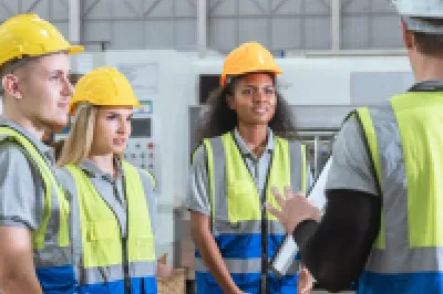 Three workers in hard hats, safety vests, and protective gear discussing at an industrial facility.